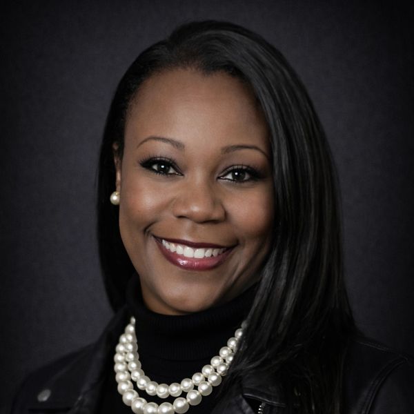 Confident woman smiling, wearing pearl jewelry and a black outfit.