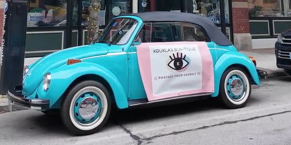 Turquoise vintage Volkswagen Beetle with a promotional sign parked on a city street.