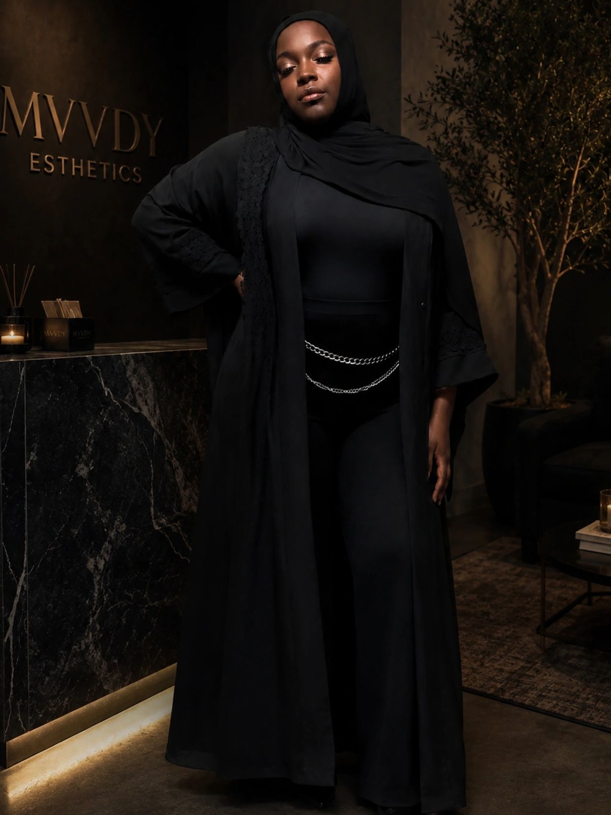 Confident woman in black abaya standing indoors with elegant decor.