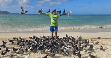 Kailua Birdman reaching out with a flock of pigeons surrounding him.