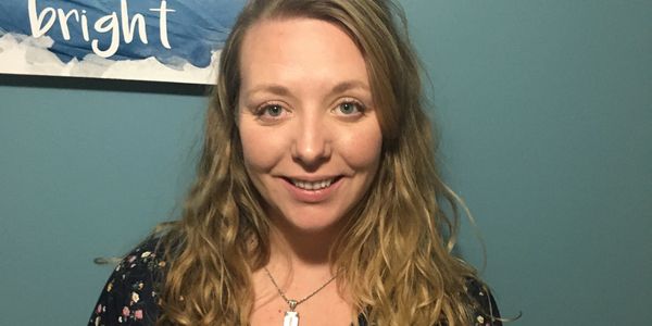 Smiling woman with wavy hair in front of a blue wall.