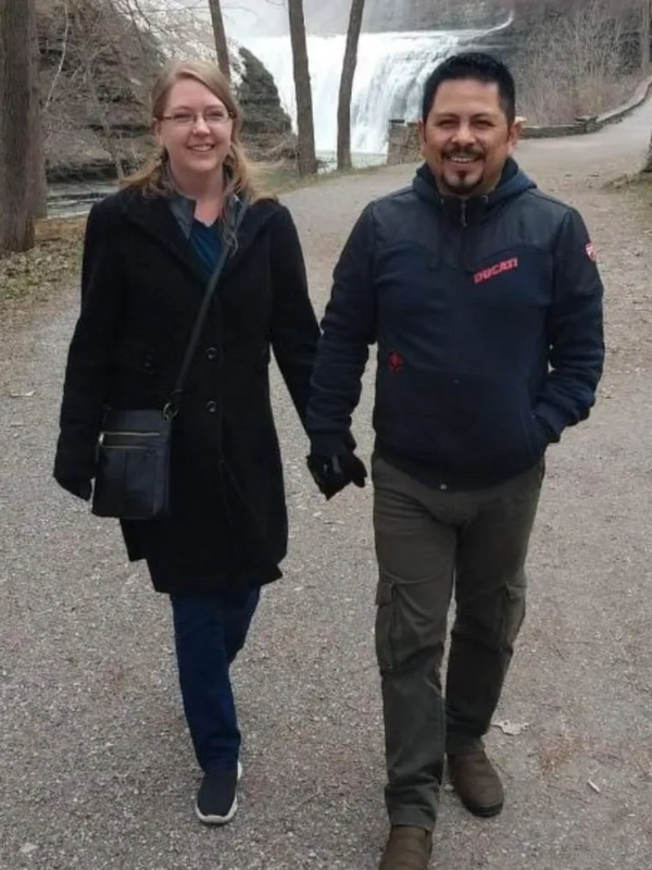 A smiling couple holding hands while walking on a path near a waterfall.