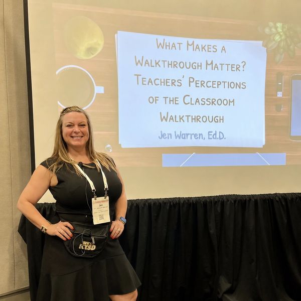 Woman stands smiling in front of a presentation slide about classroom walkthroughs by Jen Warren, Ed.D.
