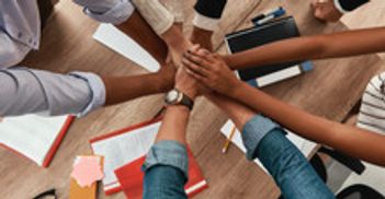 Team members joining hands in a collaborative gesture over a desk.