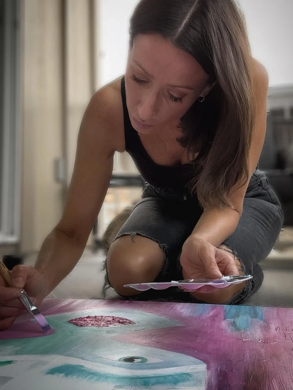 A woman holding a paintbrush and palette, painting a colourful image with acrylic paint on canvas