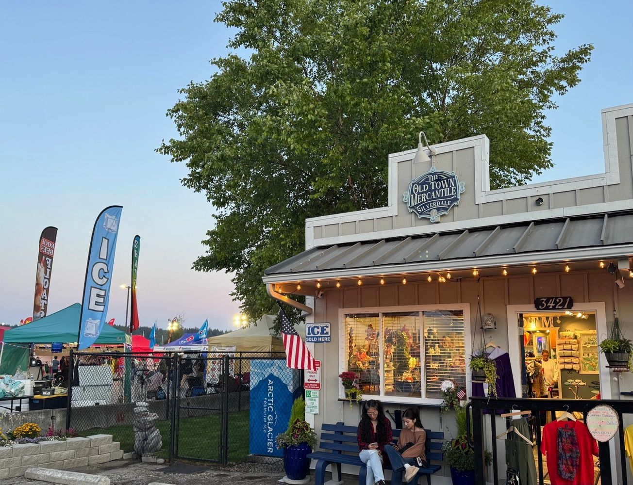 Two people sitting outside The Old Town Mercantile during a lively outdoor event.