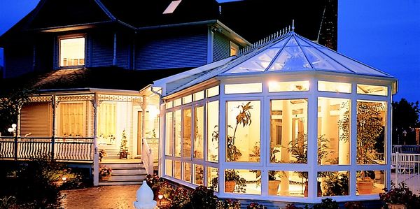 Beautiful glass conservatory glowing warmly at night beside a Victorian-style home and garden.
