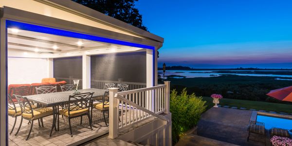 Luxurious screened porch with blue LED lighting at dusk, overlooking a vast body of water and landsc