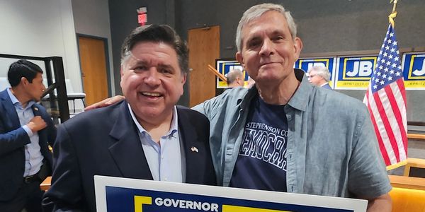 Two men smiling, holding a signed campaign sign for Governor JB Pritzker.
