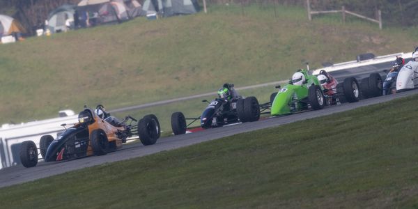 Several open-wheel race cars compete on a curved track during a race.