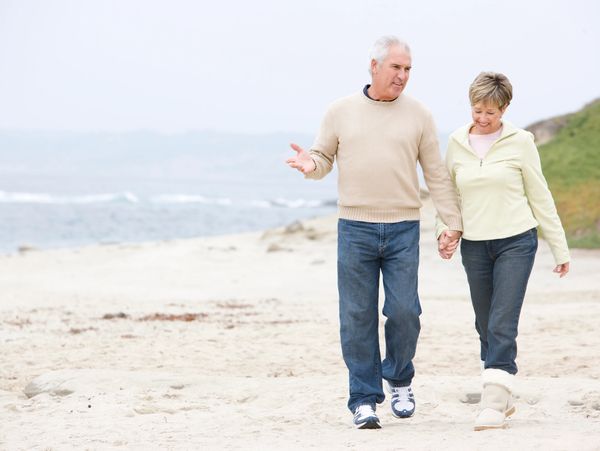 retired couple holding hands walking on the beach