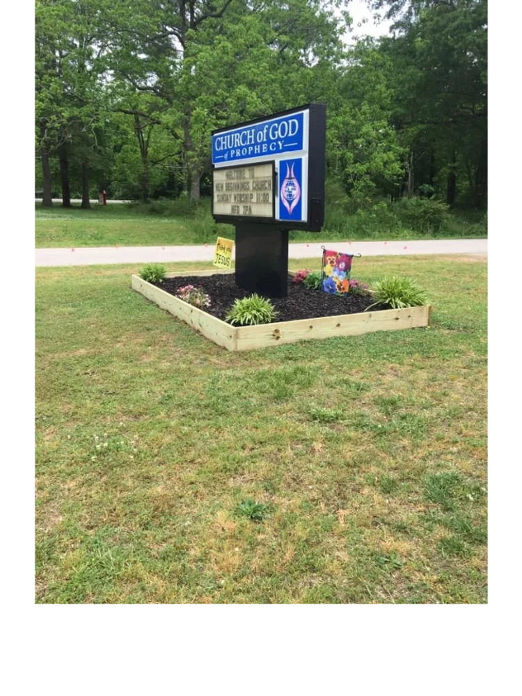 Church of God Prophecy sign in a landscaped garden bed with flowers and greenery.