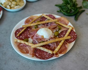 Charcuterie plate with salami, prosciutto, olives, breadsticks, and burrata cheese.