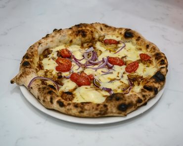 Neapolitan pizza with melted cheese, cherry tomatoes, and red onions.