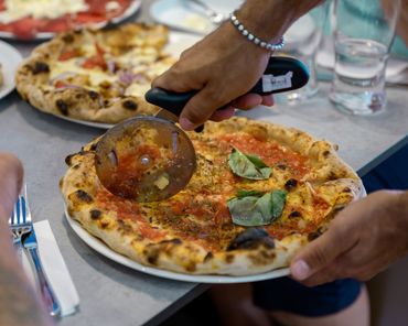 Person cutting a Margherita pizza with a pizza wheel.
