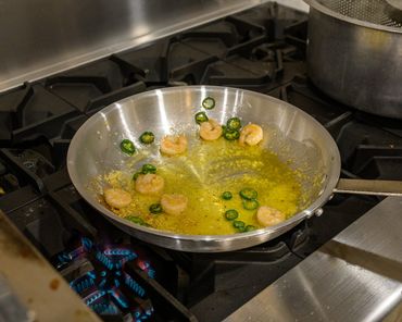Shrimp and sliced jalapeños cooking in a buttered pan on a stove.
