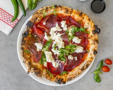 Rustic pizza topped with arugula, cured meat, and dollops of creamy cheese.