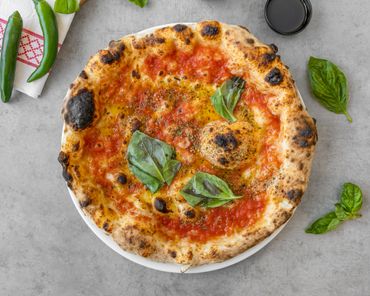 Neapolitan-style pizza with charred crust, tomato sauce, and fresh basil leaves.