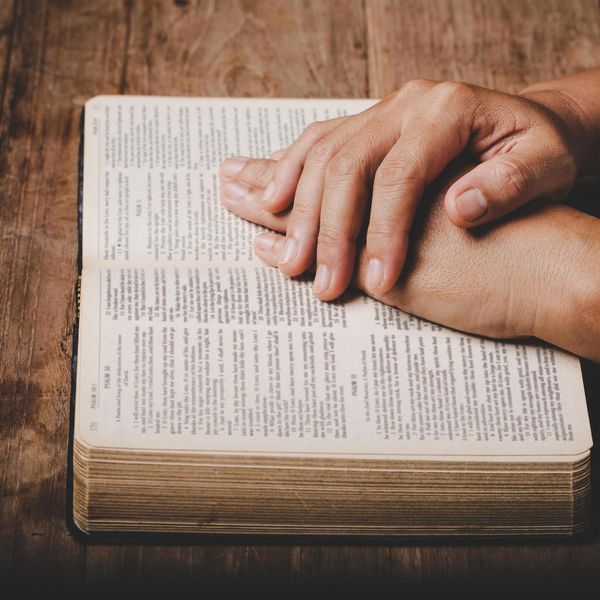 Hands resting on an open book, symbolizing prayer or reflection.