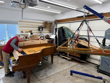 Man repairing a grand piano in a well-equipped workshop.