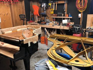 Disassembled grand piano in a workshop with tools and equipment.