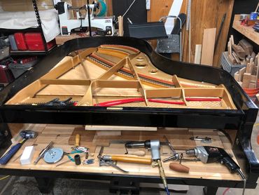 A grand piano frame being repaired with tools laid out in a workshop.