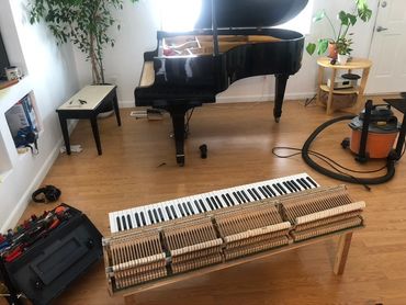 A grand piano undergoing repair with keys and hammers removed and tools nearby.