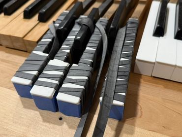 Close-up of piano keys with some keys wrapped in rubber bands on a wooden surface.