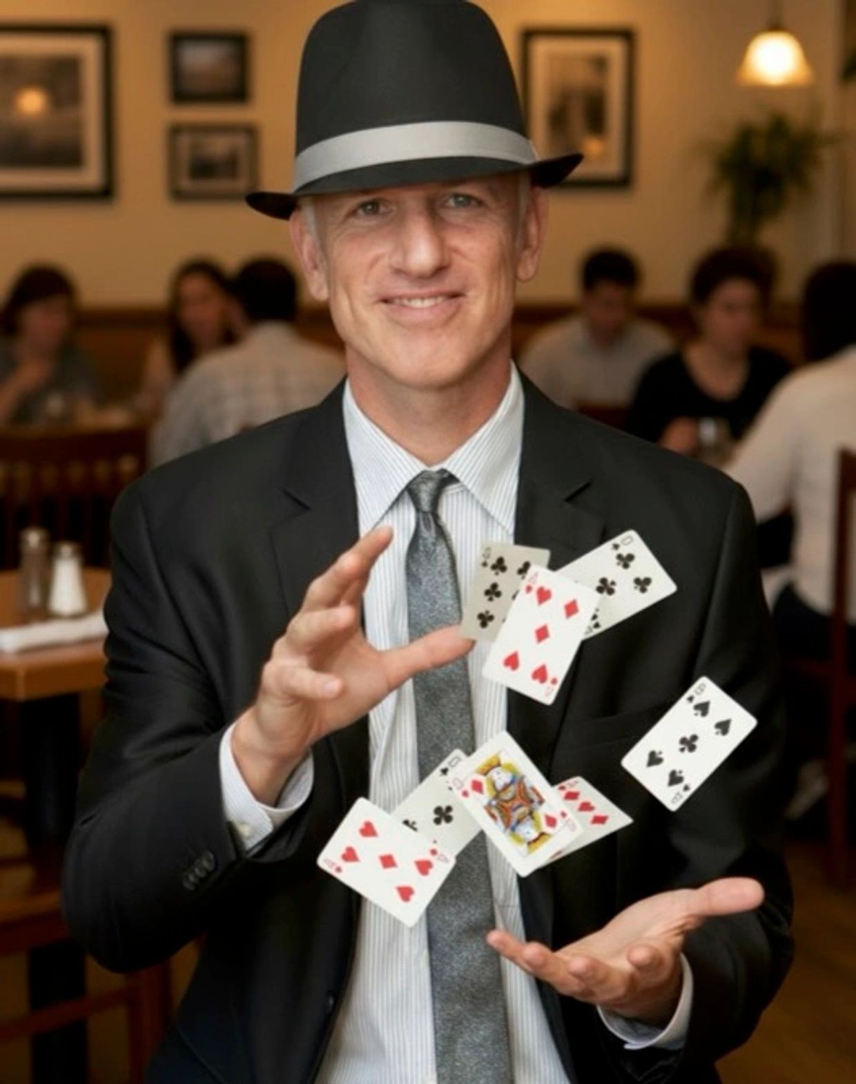 Magician in a suit and hat performing a card trick with floating playing cards.