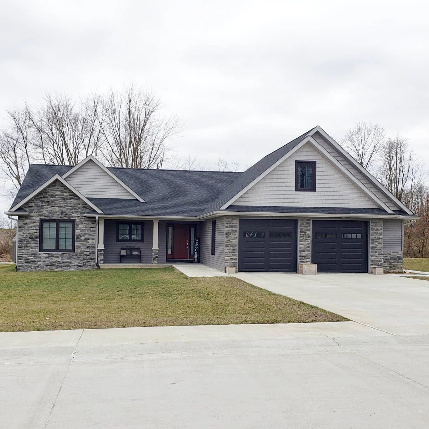 Gray sided house with stone accents, black windows, black garage doors, red entry door.