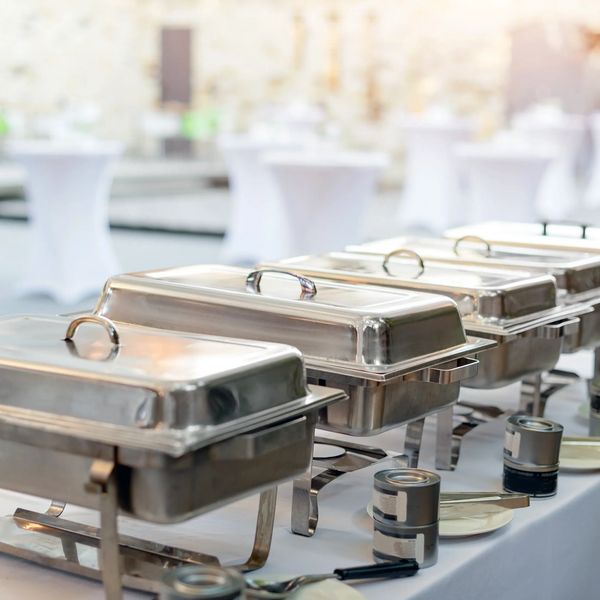 A row of covered chafing dishes set up for event catering on a buffet table serving local sourcing vegan catering/plant based catering.