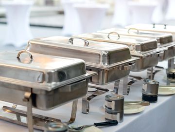 A row of covered stainless steel chafing dishes on a buffet table.