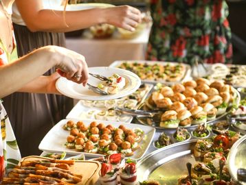 People serving themselves from a lavish buffet with various appetizers and mini sandwiches.