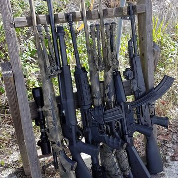 Multiple bolt action and semi-automatic rifles lined up on a rifle gun rack.