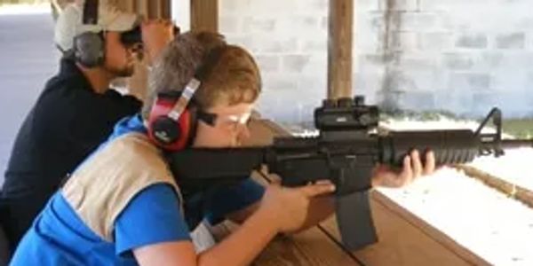 Young kid shooting an AR-15 at the rifle range with an instructor.