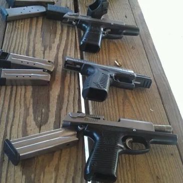 Multiple revolvers and semi-automatic pistols lined up on the shooting bench.