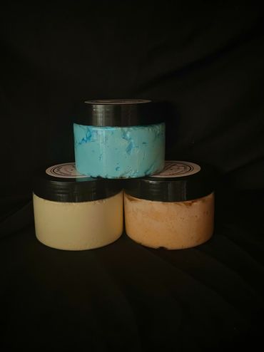 Three jars with black lids containing different colored creams against a black background.