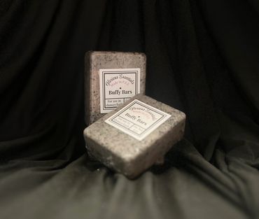 Two speckled Buffy Bars soap bars on black fabric background.