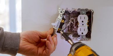 Hand wiring a wall outlet in an electrical box with a screwdriver—outlet and light-switch additions.