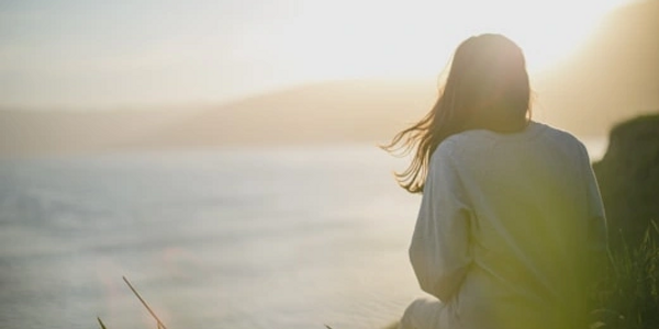 A person in a sweater enjoying a serene sunset by the water.