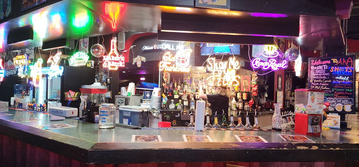 Neon-lit bar counter with various drinks and menus.