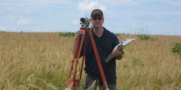 Agronome qui prend les niveaux pour l'aménagement d'une voie d'eau engazonnée à Lefebvre