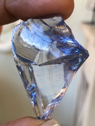 Close-up of a translucent blue crystal held between fingers.