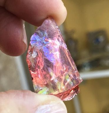 Close-up of a hand holding a colorful iridescent crystal shard.