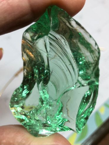 Close-up of a translucent green glass shard held between two fingers.