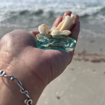 Hand holding seashells and a piece of blue sea glass on the beach.