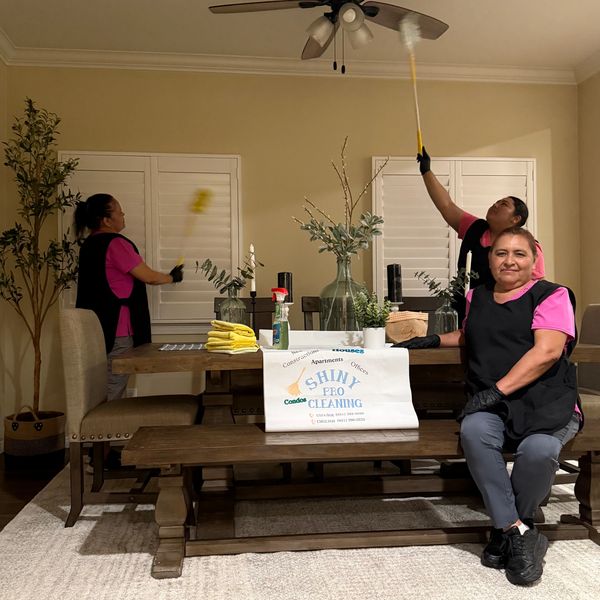 3 Mexican ladies cleaning a dining room. Wearing black pants, pink shirt and black apron.