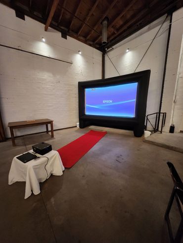 Indoor setup with inflatable projector screen and red carpet.