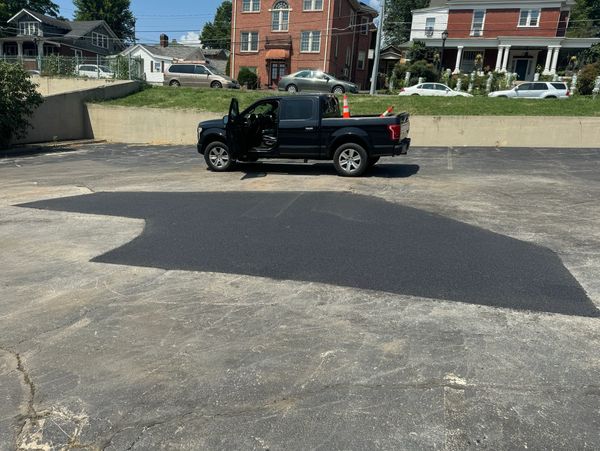 A black pickup truck with an open door parked on a freshly paved asphalt patch.