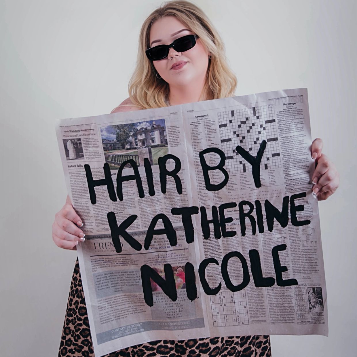 Woman holding newspaper with "Hair by Katherine Nicole" written on it.